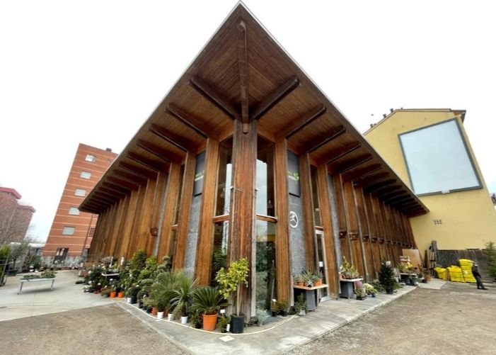 Foto dall'esterno della costruzione in cui si è tenuto l'evento. La costruzione sembra essere in legno, si vedono delle piante fuori e dentro.